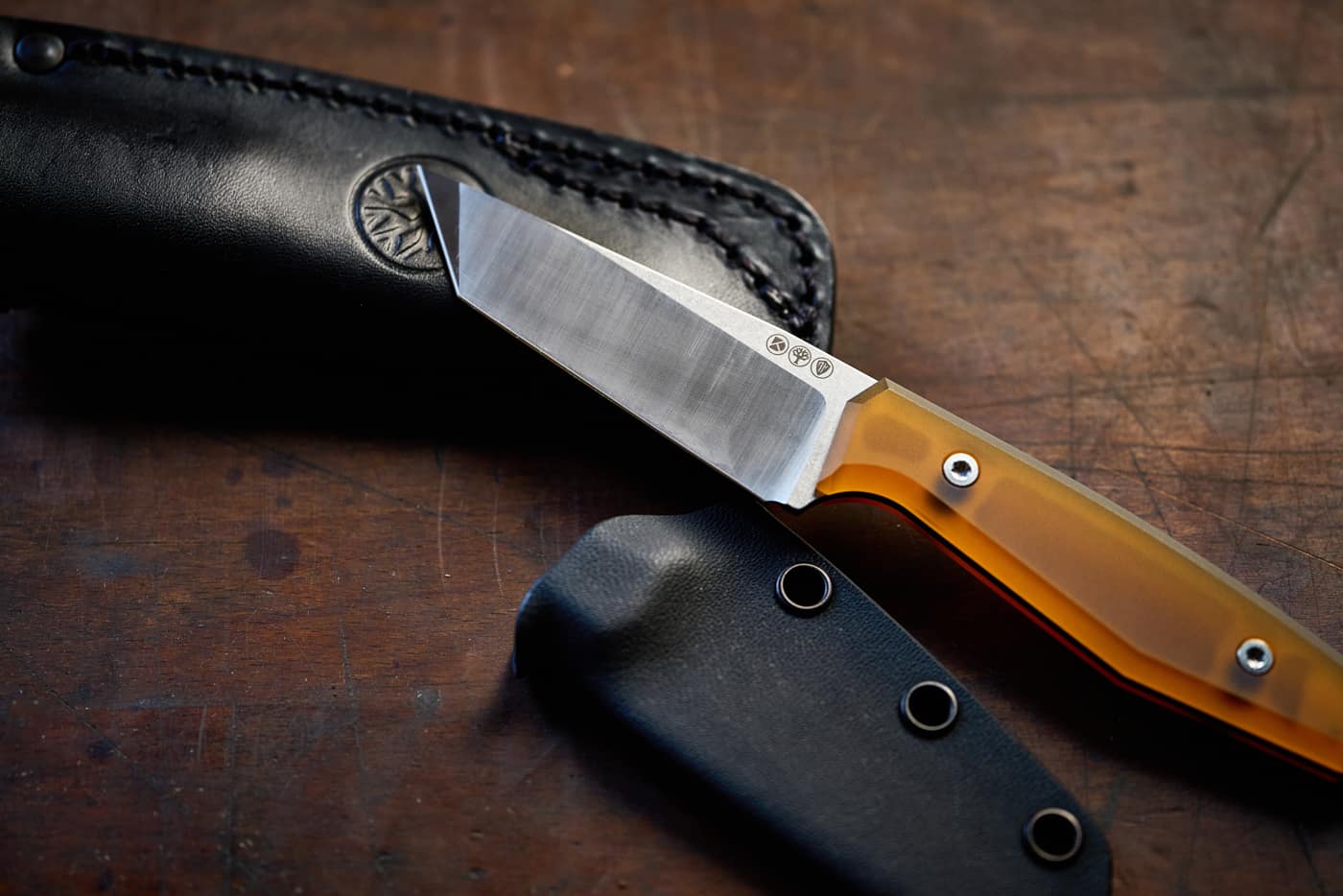 Rostfreies Messer mit orangefarbenem Griff, daneben liegen eine Lederscheide und eine Kydexscheide