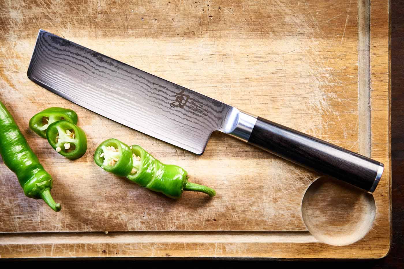 Ein japanisches Nakiri Messer auf einem Holzbrett. Daneben eine geschnittene Peperoni.